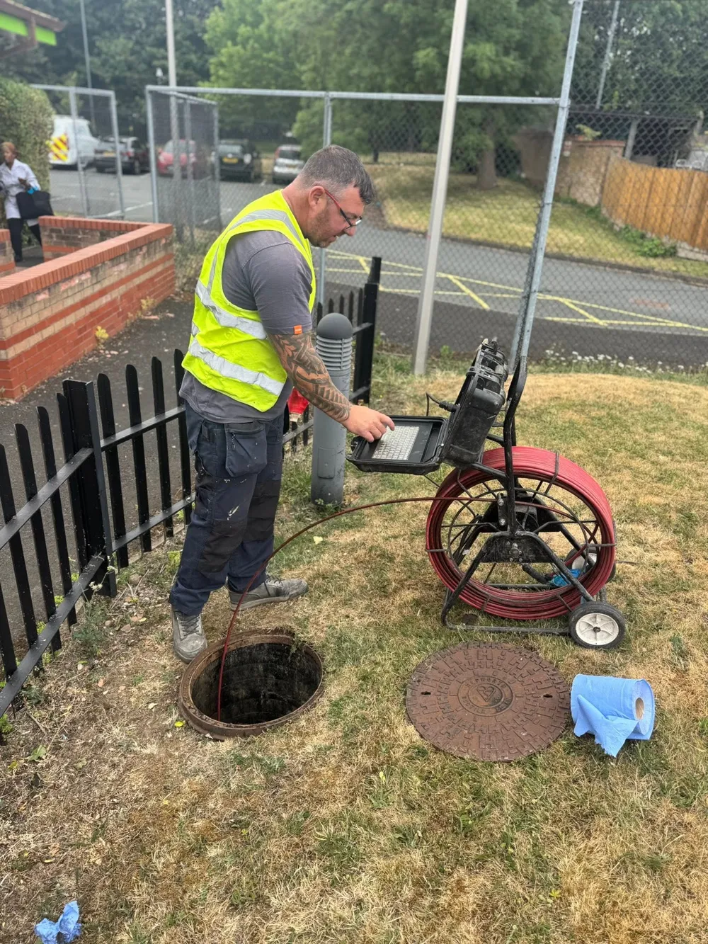Drainage operative using a CCTV camera reel and inspection monitor beside an access chamber